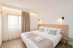 A hotel room with two beds, a small table, and a window with curtains. - Ereza Residence 3 in Arrecife (Arrecife)