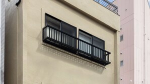 Ein Gebäude mit einer beigefarbenen Fassade, zwei Balkonen mit schwarzen Geländern und einem Rundfenster. Ein Schild trägt die Aufschrift 'Yamazaki'.