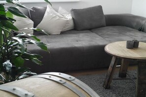 Ein modernes Wohnzimmer mit einem grauen Ecksofa, einem runden Couchtisch aus Holz und einem Blumentopf.