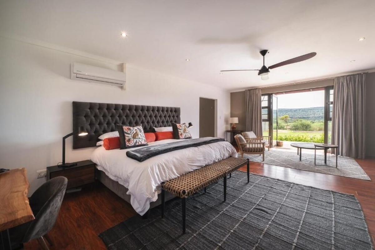 A modern bedroom with a large bed, a bench, a desk, and a chair.