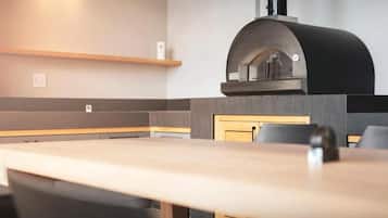 Un intérieur de restaurant moderne avec une longue table à manger, des chaises noires et un four à pizza encastré.