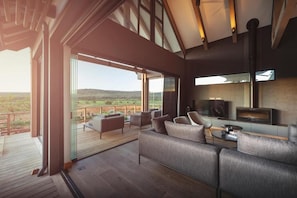 A modern living room with a large sofa, a television, and a wooden deck with outdoor seating. - Ufumene Game Lodge (Alicedale)