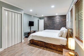 Ein Schlafzimmer mit Bett, Fernseher, Schreibtisch und einem Fenster mit Jalousien.