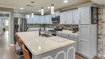 Une cuisine moderne dotée d’un grand îlot central, d’appareils électroménagers en acier inoxydable et de luminaires suspendus.