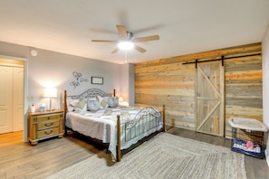 Ein Schlafzimmer mit einem Bett, Nachttischen, einer Kommode, einem Deckenventilator, einer Holzwand und einer Schiebetür im Bauernhausstil.