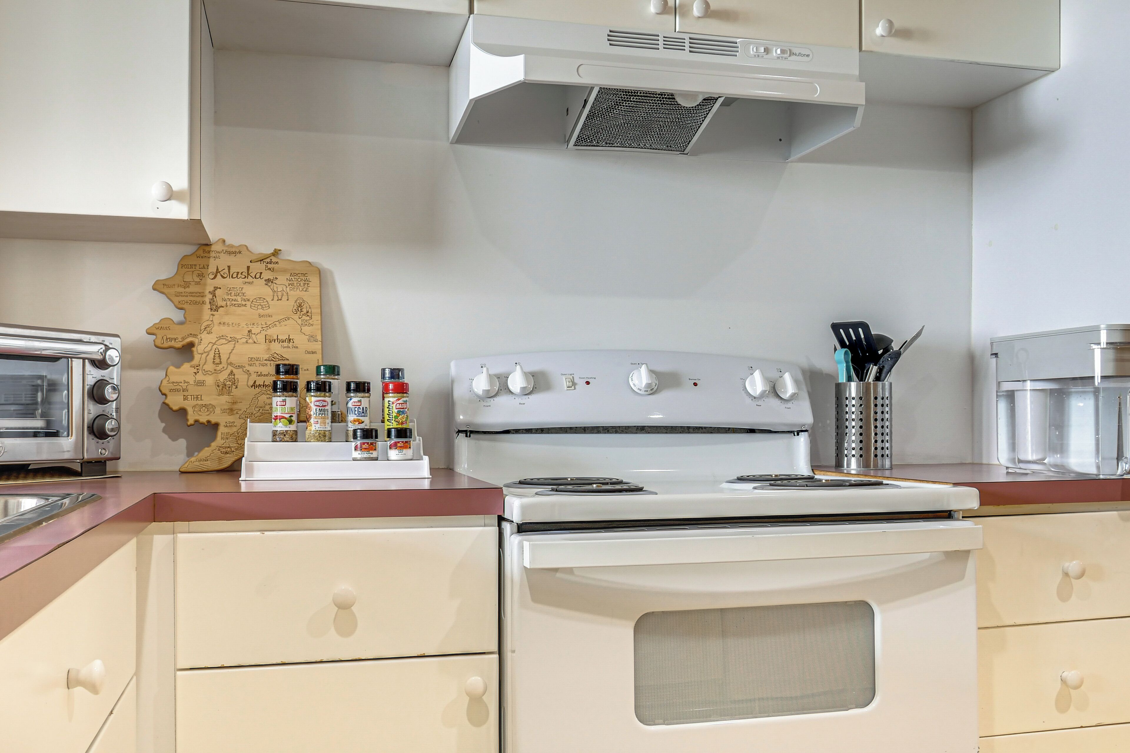 A kitchen with a white stove, a toaster, and a map of Alaska on the counter.