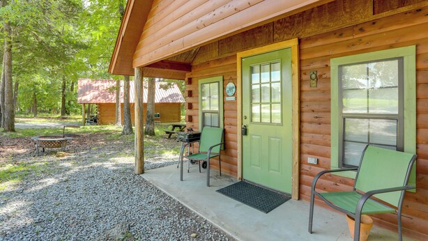 Una cabaña de troncos con una puerta verde, dos sillas verdes afuera y una mesa de picnic.