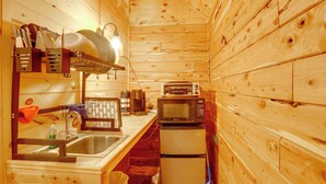 Una cocina compacta con paredes de madera, un lavamanos, un microondas y un refrigerador pequeño.