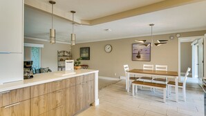 A modern kitchen with wooden cabinets, a white countertop, and a dining area with a wooden table and white chairs. - Boat Dock & Lift! North Fort Myers Family Getaway (North Fort Myers)