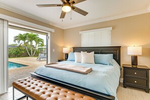 Ein Schlafzimmer mit Bett, Nachttischen, Deckenventilator und Blick auf einen Swimmingpool.