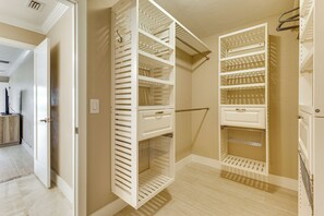 Een inloopkast met open planken en lades, een kledingroede en een deur naar een andere kamer.
