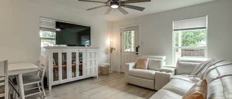 A living room with a white sofa, a dining table with chairs, a TV, and a ceiling fan.