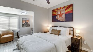 A bedroom with a bed, a chair, a nightstand, a lamp, a ceiling fan, and a wall with a poster. - Historic Prescott Gem! Walk to Whiskey Row! (Prescott)