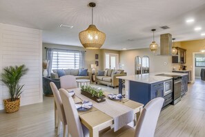Eine moderne Küche mit einer zentralen Kochinsel, einem Essbereich mit Stühlen und Tisch sowie einem Wohnbereich mit Sofa und Couchtisch.