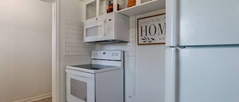 A compact kitchen with white appliances, including a microwave, oven, and refrigerator, with a 'happy to be HOME' sign above the microwave.