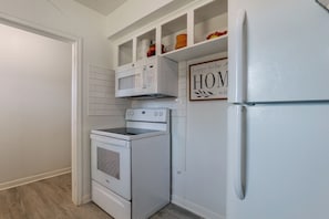 A compact kitchen with white appliances, including a microwave, oven, and refrigerator, with a 'happy to be HOME' sign above the microwave. - Suburban Sanctuary: Magnolia Home w/ Backyard! (Magnolia)