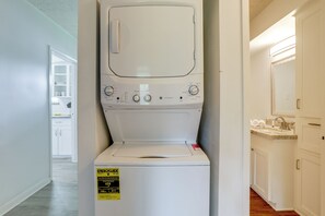 Eine weiße Waschmaschine und ein Trockner mit ENERGY GUIDE-Aufkleber, ein Küchenbereich mit Spüle und Schränken sowie ein Flur, der zu einem Raum mit einer Tür führt.