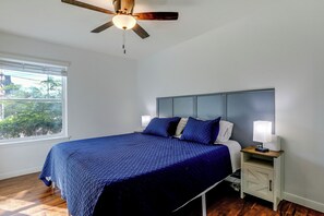 A bedroom with a bed, a nightstand, a ceiling fan, a window, and a view of greenery outside. - Suburban Sanctuary: Magnolia Home w/ Backyard! (Magnolia)