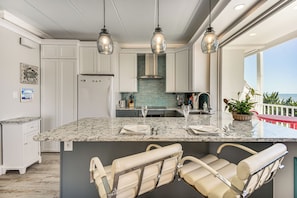 A kitchen with a large island, white cabinetry, and pendant lighting.