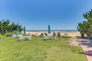 A grassy area with outdoor seating and umbrellas, a pathway leading to the beach, and a view of the ocean.