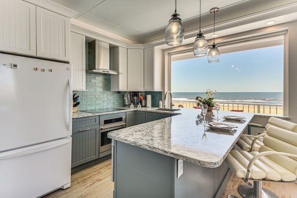 A kitchen with a large island, a view of the ocean, and a balcony with seating.