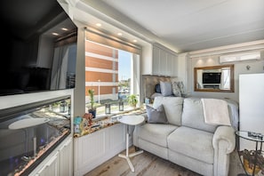 A compact living space with a kitchenette, a sofa, a small table, and a window with a view of the outside.