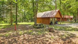 Uma cabana com mesa de piquenique e lareira em área arborizada.