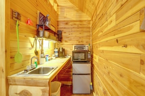 Une cuisine de taille réduite, équipée d’un évier, d’un four à micro-ondes et d’un réfrigérateur, avec des murs en bois et un balai.