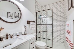 Un baño con un lavamanos blanco, un inodoro, una ducha con puertas de vidrio y un espejo con marco circular.