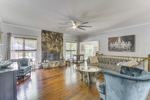 A spacious living room with a stone wall, a ceiling fan, a large sofa, and a TV. - Gateway to St Louis: Group Getaway w/ Game Room (Florissant)