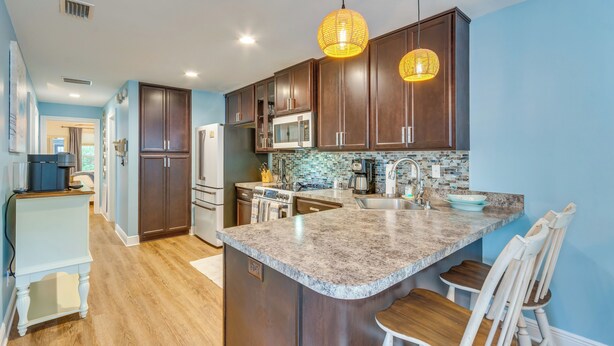 A modern kitchen with dark wood cabinets, granite countertops, a central island, and pendant lighting. - Downtown Gem: Walk to Restaurants & Palafox St! (Pensacola)