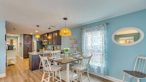 A modern kitchen with wooden cabinets, a dining table with chairs, pendant lights, and a view to the living area. - Downtown Gem: Walk to Restaurants & Palafox St! (Pensacola)