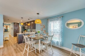 A modern kitchen with wooden cabinets, a dining table with chairs, pendant lights, and a view to the living area. - Downtown Gem: Walk to Restaurants & Palafox St! (Pensacola)