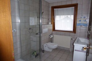 Kylpyhuoneessa on lasiseinäinen suihkukaappi, wc-istuin, pesuallas ja puukehysikkuna.