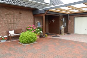Ein Backsteinhaus mit einer hölzernen Bank, einem kleinen Garten mit Blumen und einem überdachten Eingang.