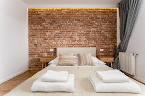 Ein Schlafzimmer mit Backsteinwand, einem Bett mit weißer Bettwäsche, zwei Nachttischen und einem Heizkörper.