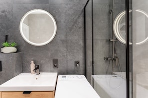 Ein modernes Badezimmer mit einem runden Spiegel, einem Waschbecken, einer Dusche und einer Toilette.