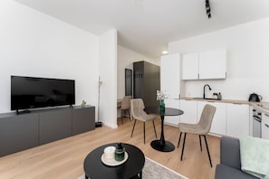 Ein modernes Wohnzimmer mit Flachbildfernseher, Essbereich mit Stühlen, Küche mit Schränken und ein kleiner Tisch mit einer Vase.