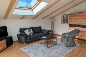 A modern loft bedroom with a skylight, a dark sofa, a wicker chair, and a wooden wardrobe. - Apartment in Walchensee with swimming pool (Walchensee)