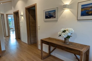 A hallway with wooden flooring, a wooden console table with a vase of white flowers, and framed pictures on the wall. - Apartment in Walchensee with swimming pool (Walchensee)