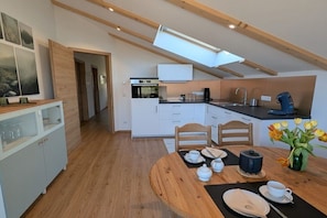 A modern kitchen with white cabinets, a wooden dining table set for two, and a skylight above. - Apartment in Walchensee with swimming pool (Walchensee)