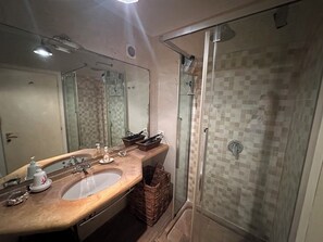Une salle de bain avec un grand miroir, un lavabo, une douche dotée d’une porte en verre et un mur de douche recouvert de carreaux.