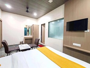 A hotel room with a bed, a desk, two chairs, a TV, and a window. - Hotel Royal Inn (Panvel)