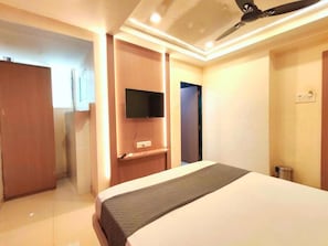 A hotel room with a bed, a flat-screen TV mounted on the wall, a ceiling fan, and a small trash bin. - Hotel Royal Inn (Panvel)