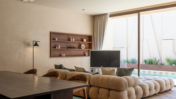 Una sala de estar moderna con sofá, televisor, mesa de comedor y lámpara colgante.