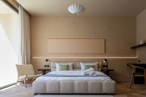 Moderni hotellihuone, jossa on suuri sänky, yöpöytä, tuoli ja näkymä ulos.