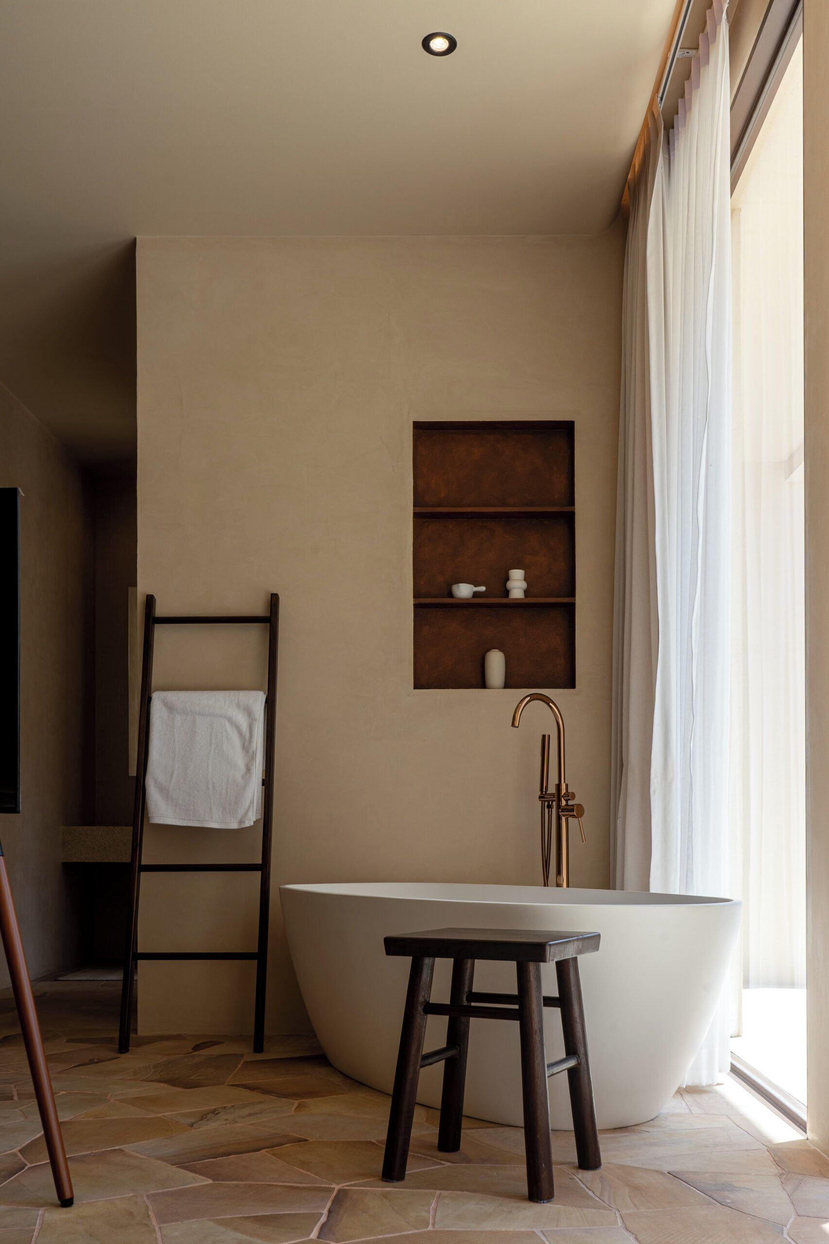Ein Badezimmer mit freistehender Badewanne, einer Holzleiter, einem Handtuchhalter und einem Ablagebereich mit Toilettenartikeln.