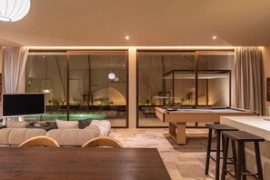 Ein modernes Wohnzimmer mit Billardtisch, Flachbildfernseher und einer Couch.