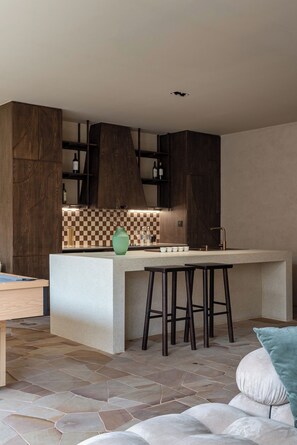 Cozinha moderna com área de bar, piso de pedra e armários de madeira.
