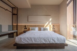 Quarto moderno com cama grande, cabeceira de madeira, mesas de cabeceira e um banquinho.